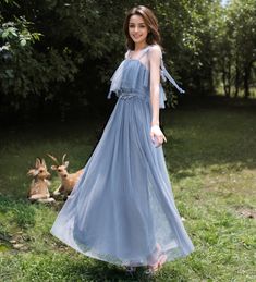 a young woman in a blue dress standing on the grass next to a deer laying down