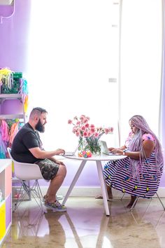 a man and woman sitting at a table in front of a vase with flowers on it