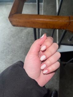 a woman's hand with white and pink manicures on it, sitting in front of a wooden chair