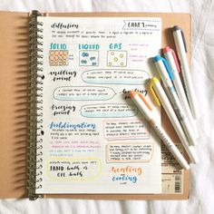 an open notebook with writing and markers on it, next to some pencils that are laying on top of each other