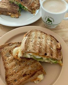 a sandwich cut in half on a plate next to a cup of coffee