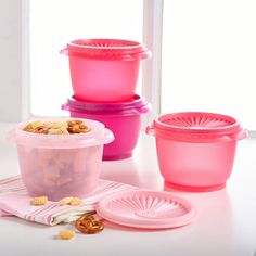 four plastic containers with lids and plates on a white countertop next to a window