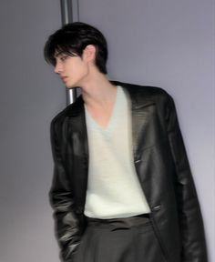 a man in a black leather jacket and white shirt standing next to a gray wall