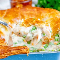 a spoonful of chicken pot pie is being lifted from a blue casserole dish