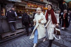 two women are walking down the street in front of some people and one is carrying shopping bags