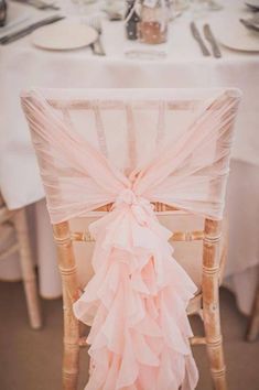 the back of a chair covered in pink ruffles at a table with plates and utensils