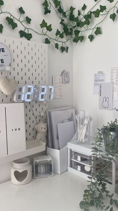 a white desk topped with lots of clutter and office supplies next to a plant