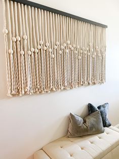 a white bench sitting next to a wall covered in macrame balls and tassels