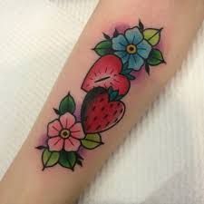 a strawberry and flower tattoo on the arm with flowers around it's center piece