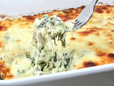 a fork is lifting some food out of a casserole dish with cheese and spinach