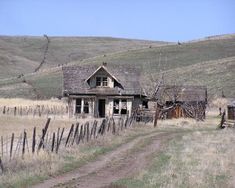 an old run down house in the middle of a field with a dirt path leading to it