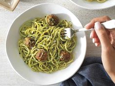 a person is eating spaghetti with meatballs in a white bowl on a wooden table