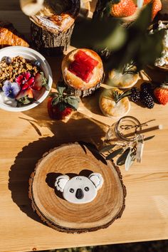 a wooden table topped with lots of fruit and pastries next to a bowl of berries