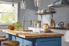 a kitchen with blue cabinets and wooden counter tops next to a stove top oven under hanging lights