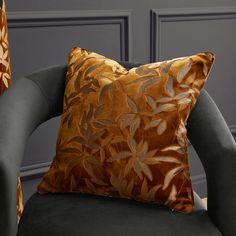 an orange and brown pillow sitting on top of a black chair next to a gray wall