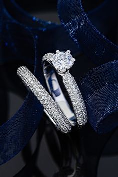 two wedding rings on top of each other in front of blue ribbon and sequins