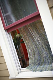 an open window with a knitted blanket hanging from it's side, in front of a house