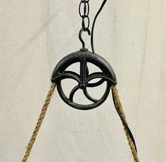 an old fashioned black clock hanging from a chain on a white wall with rope around it