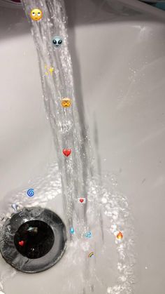 a faucet running out of a sink filled with water and smiley face stickers