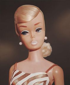 a barbie doll with blonde hair wearing a white and brown striped dress, earrings and necklace