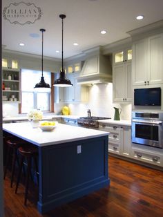 a kitchen with white cabinets and blue island in the center is lit by two pendant lights