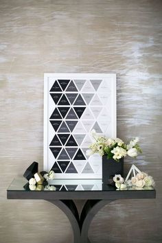 a black and white table with flowers on it next to a framed art piece that has geometric designs