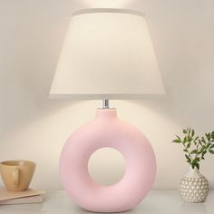 a pink lamp sitting on top of a table next to a white vase with a plant in it