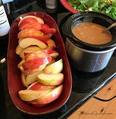 apples and other fruits are in bowls on the counter next to an open crock pot