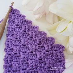 a crocheted purple piece of cloth next to white flowers