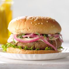 a hamburger with onions and lettuce on a white plate next to a glass of orange juice