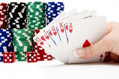 a hand holding four playing cards in front of stacks of poker chips and dices