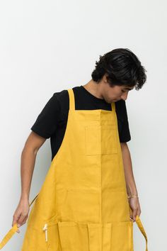 a young man wearing an apron and black t - shirt is holding a yellow object in his right hand