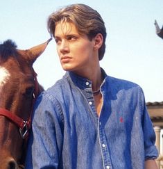 a young man standing next to a brown horse