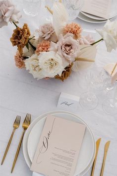 the table is set with white and gold place settings, silverware, and flowers