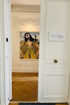 A view through a doorway to Jenny Packham's Paris Atelier, for Paris Fashion Week September 2022. On the wall through the door is a glimpse of the painting 'Ready or Not' by Veronica Wells, commissioned by Jenny Packham especially. Bond Girl, The Duchess