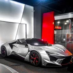 a silver sports car parked in front of a red and white wall with lights on it