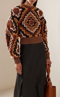 a woman wearing a brown sweater and black skirt holding a handbag in front of her face