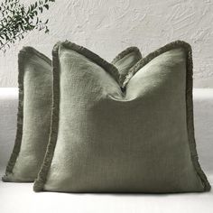 two green pillows sitting on top of a white couch next to a potted plant