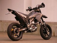 a silver motorcycle parked on the side of a road next to a white building and cement wall