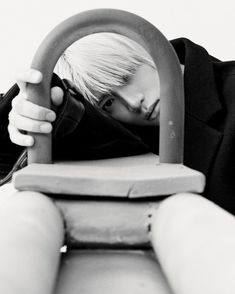 a boy with blonde hair sitting on a bench and holding an umbrella over his head