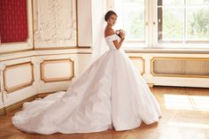 a woman in a white wedding dress standing by a window