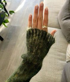 a woman's hand with a ring on it, wearing a green knitted mitt