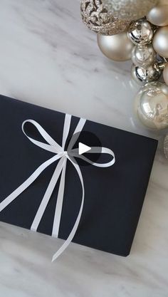 a black gift box wrapped in white ribbon with ornaments around it on a marble surface