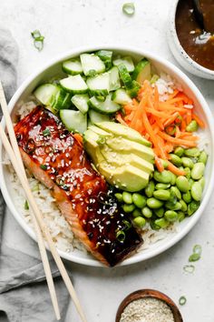 a bowl filled with rice, cucumber, carrots and other vegetables next to chopsticks