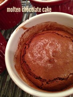 chocolate cake in a white bowl on top of a cooling rack with red cups behind it