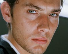 a close up of a person wearing a suit and tie with blue eyes looking at the camera