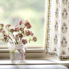 a vase filled with flowers sitting on top of a window sill next to a curtain