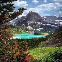 a lake surrounded by trees and mountains under a cloudy blue sky with clouds in the background