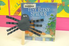 a spider made out of construction paper on top of a wooden stick in front of a book