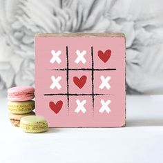 a pink tic - tac board with hearts and crosses on it next to two macaroons